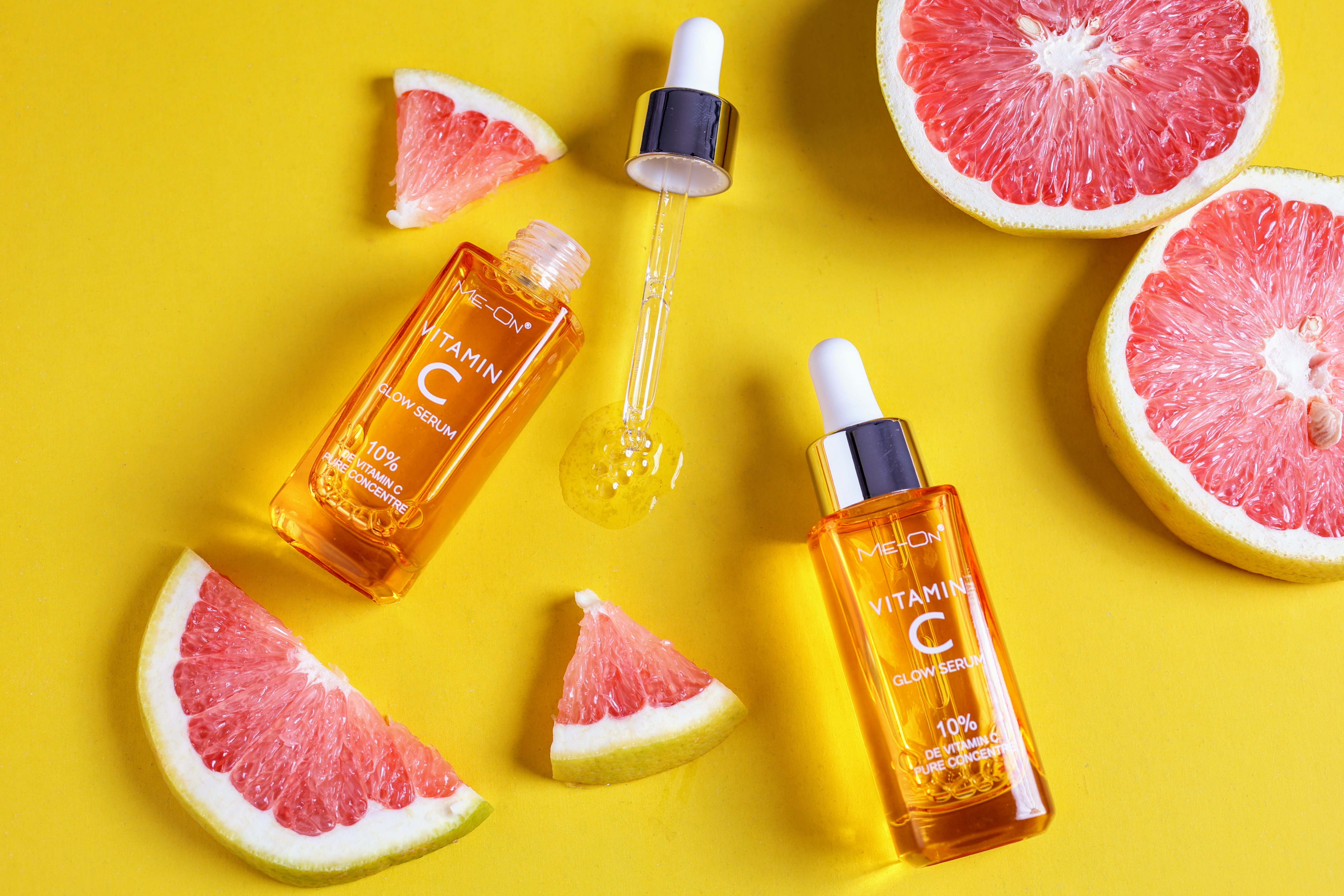 Vitamin C serum bottles with dropper and citrus slices on yellow background